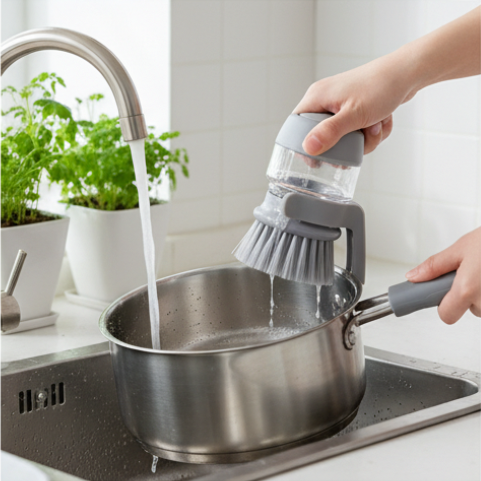 Person using a dish brush to clean a pot under running water in a kitchen.